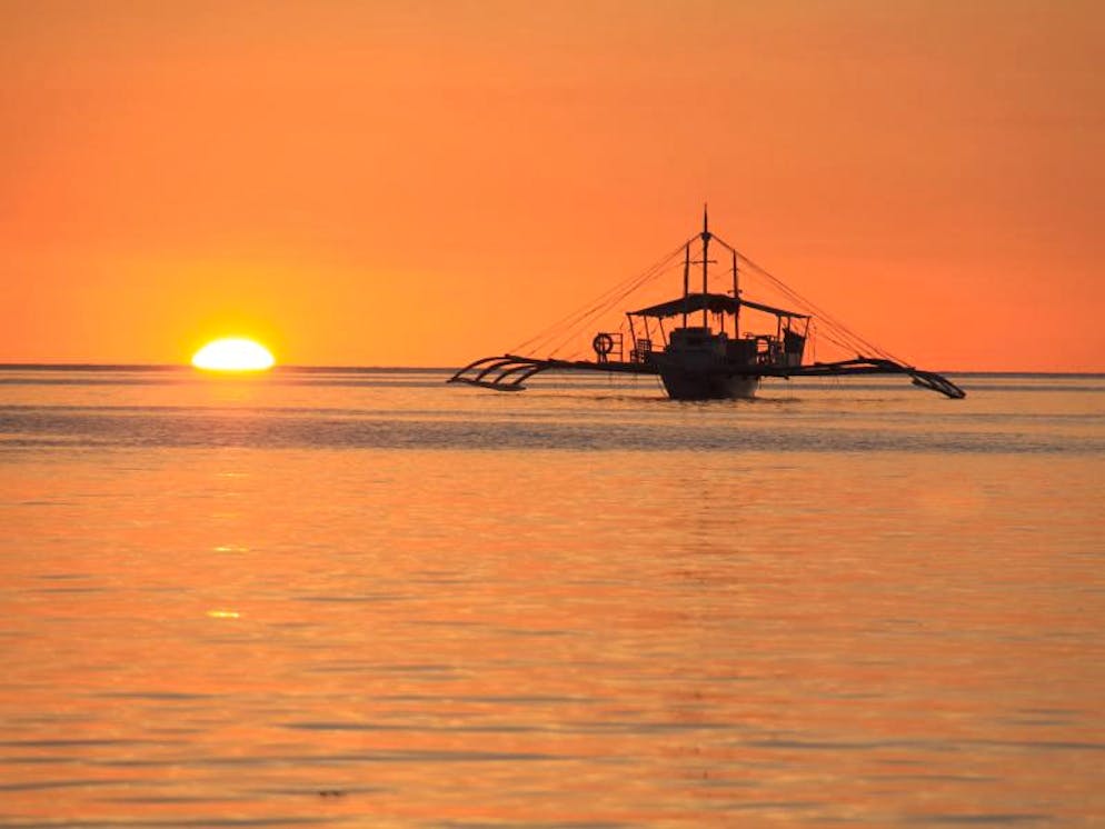 Wie eine Filmkulisse: Inselhüpfen rund ums paradiesische Palawan. Postkartenidylle bei El Nido: Eine Bangka im Sonnenuntergang - ein philippinisches Fischerboot mit typischen Ausleger-Stützen.
