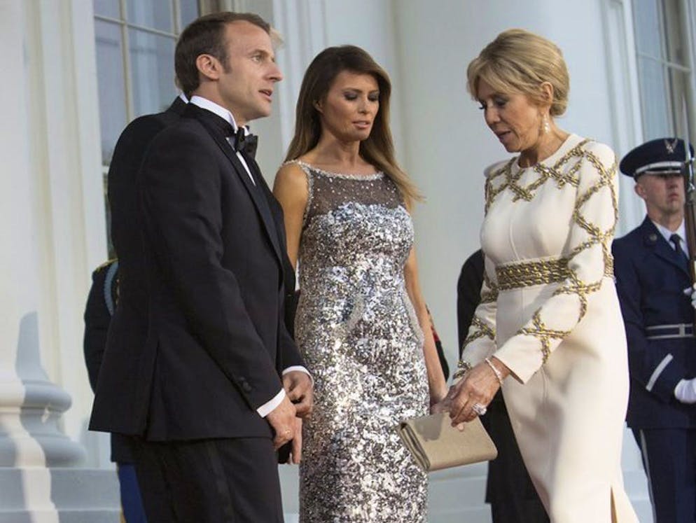 Il cappello di Melania Trump fa parlare di sé. La mise di Brigitte Macron era in perfetto accordo. La First Lady francese ha indossato un abito con motivi dorati.
