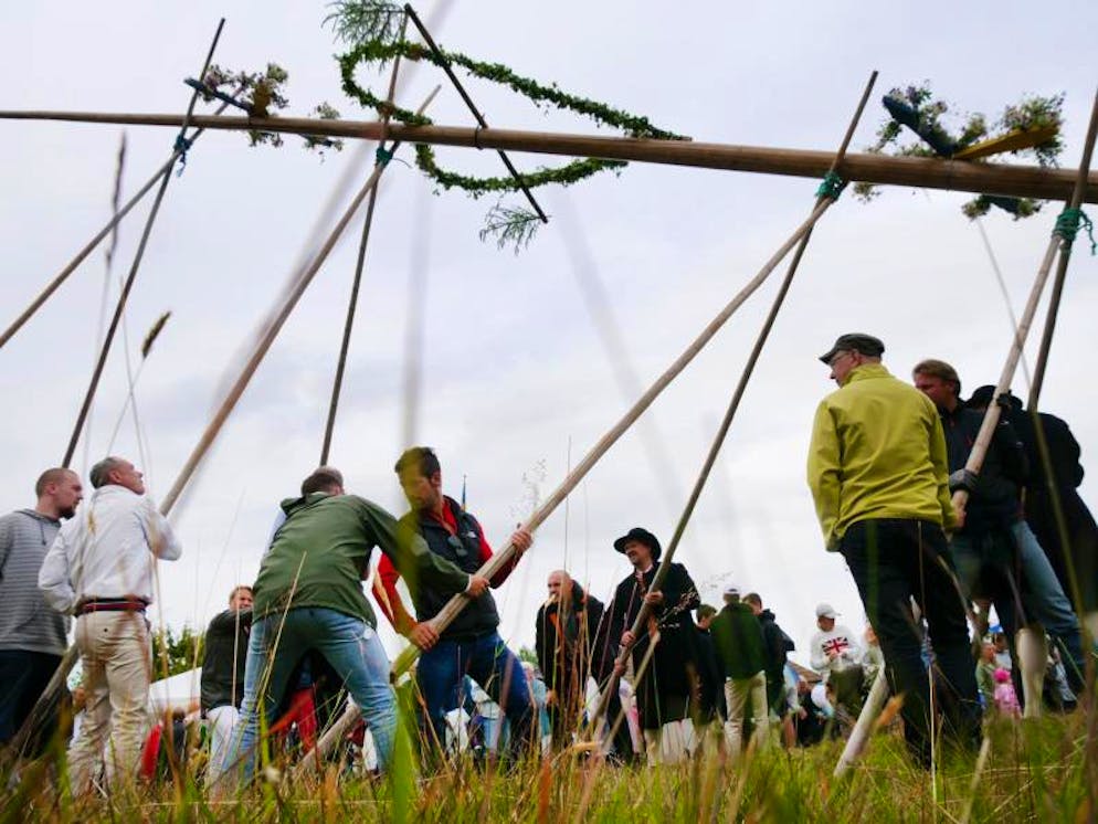 Mittsommerfest in Schweden: Blüten, Schnaps und lange Nächte. Mit Holzstangen wuchten die Männer die sogenannte «Midsommarstång» in die Höhe. Dabei müssen sie darauf achten, dass der Baum nicht zur Seite wegkippt. 