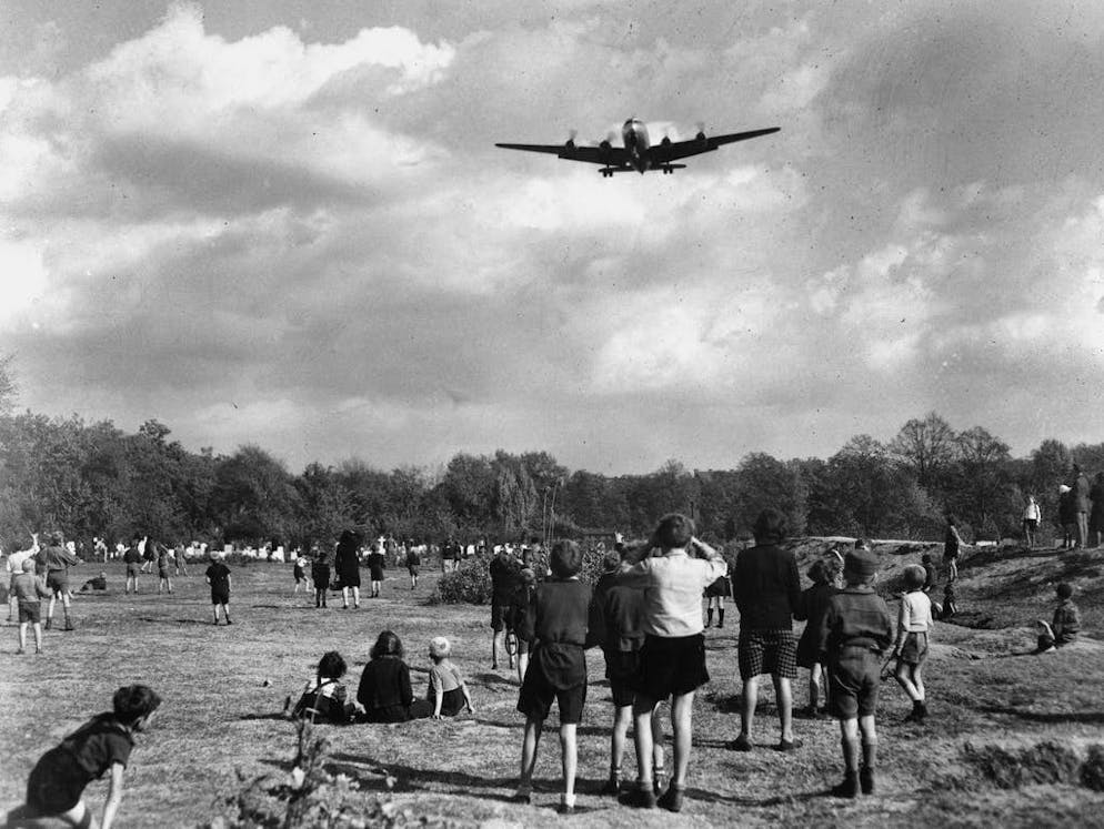 Blocco di Berlino: 70 anni fa, i «Rosinenbomber» sorvolavano la città. In questa fotografia scattata il 4 ottobre 1948, alcuni bambini berlinesi assistono all'atterraggio di un aereo da trasporto C-54 Skymaster all'aeroporto di Tempelhof.