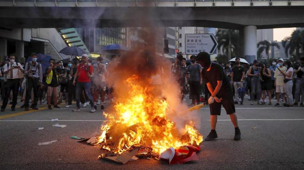 Demonstranten in Hongkong trotzen dem Vermummungsverbot. Ein Demonstrant verbrennt ein Banner zum 70. Jahrestag der Volksrepublik China. Foto: Kin Cheung/AP/dpa