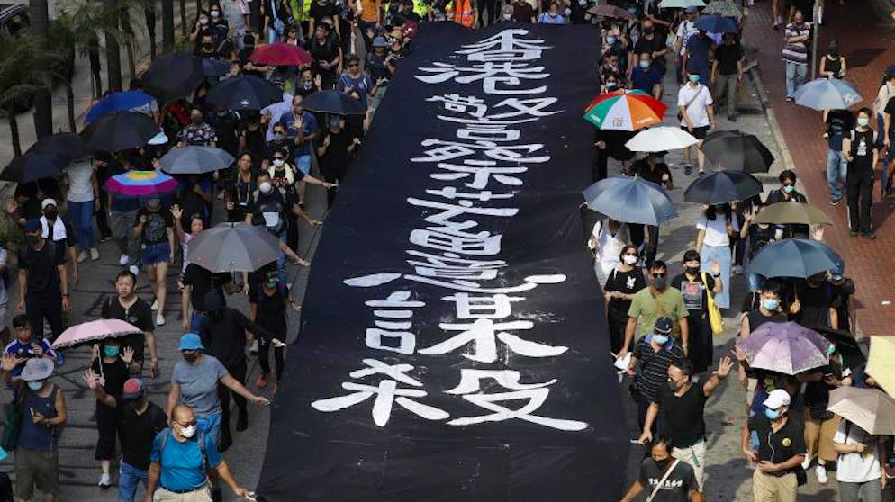 Demonstranten in Hongkong trotzen dem Vermummungsverbot. Maskierte Demonstranten neben einem Banner mit der Aufschrift «Die Hongkonger Polizei tötet absichtlich». Foto: Vincent Thian/AP/dpa