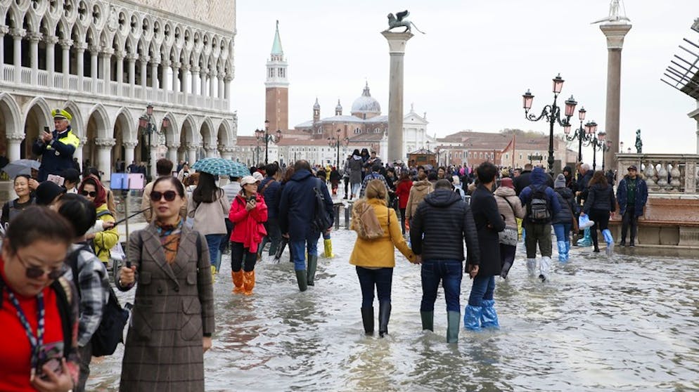 Touristen laufen auf dem überfluteten Markusplatz durch das Wasser.