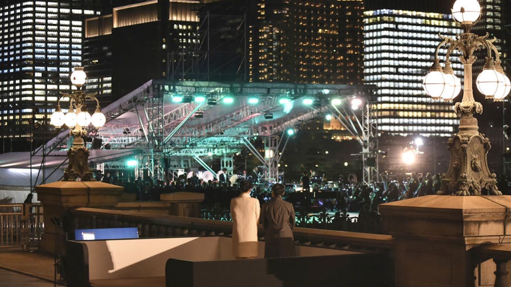 Kaiser Naruhito und Kaiserin Masako zeigen sich auf einer Steinbrücke beim Palast der fahnenschwenkenden Menge.