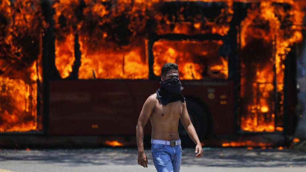 Machtkampf in Venezuela. Ein Demonstrant geht vor einem Bus, der von Gegnern des venezolanischen Präsidenten Maduro bei Zusammenstössen mit der Streitkräfte in Brand gesteckt worden ist.