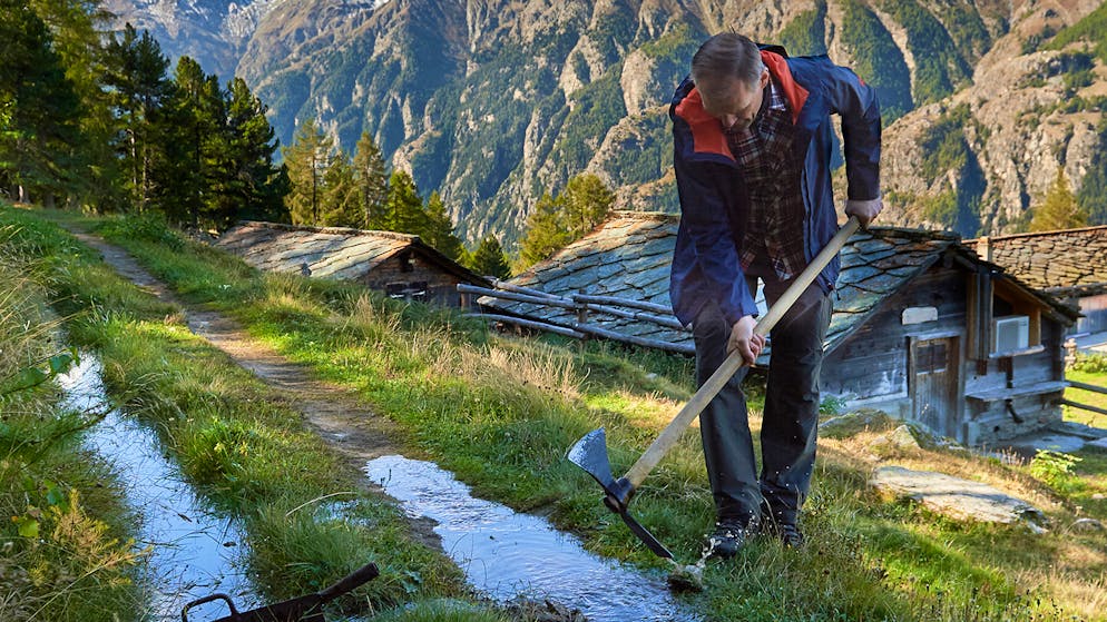 Wasserschloss Schweiz – alles im Fluss. Mit der «Wässerhouwa» schlägt er eine «Schrapfa» ins «Treschbord», und das Wasser ergiesst sich auf die unter der Suone liegenden Wiesen.