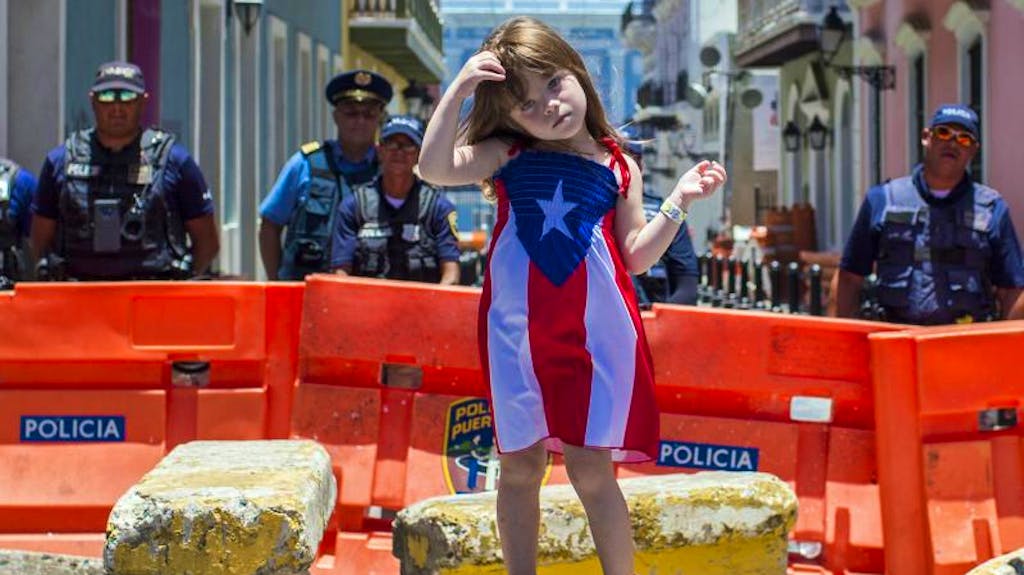 Junger Protest: Ein Mädchen in einem Puerto-Rico-Kleid nimmt an Demonstrationen in San Juan teil, während die Polizei den Weg zum Regierungspalast blockiert. Seit Tagen gehen in Puerto Rico Tausende gegen Gouverneur Rosselló auf die Strasse.