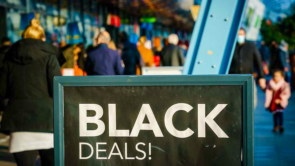 Passanten gehen vor einem Einkaufszentrum an einem Schild vorbei, das auf «Black Friday»-Angebote hinweist. Menschenmassen in Einkaufsstrassen und drohende Verstösse gegen Corona-Regeln: In den Niederlanden lehnen sich Städte gegen die Verkaufsaktion «Black Friday» auf. Foto: Marco De Swart/ANP/dpa