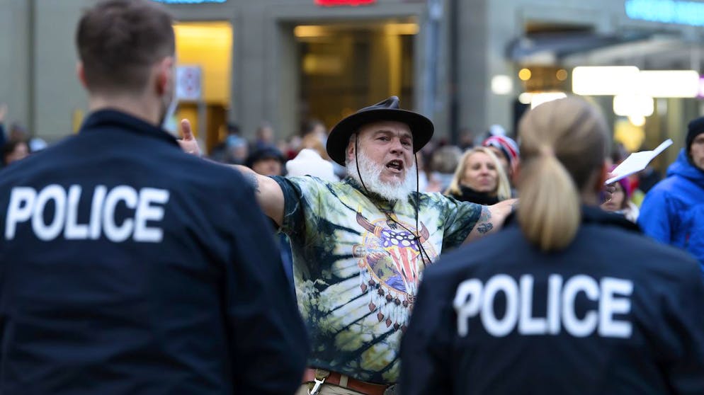 Ein Mann demonstriert gegen die Corona-Schutzmassnahmen des Bundes und wird von Polizisten ueberwacht, am Samstag, 19. Dezember 2020, auf dem Bundesplatz in Bern. (KEYSTONE/Anthony Anex)