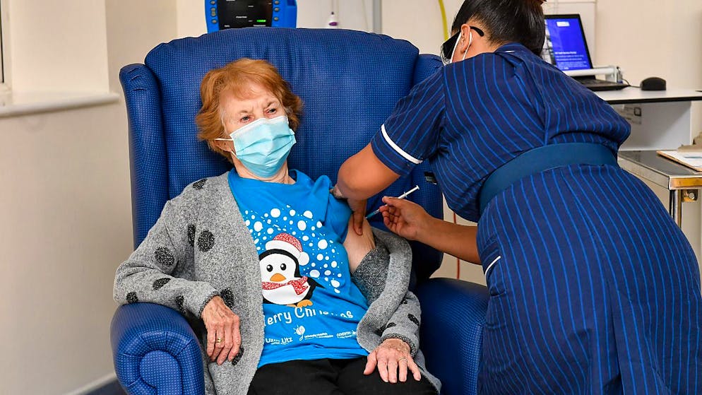 Die 90-jährige Margaret Keenan (l) bekommt im Universitätskrankenhaus Coventry von der Krankenschwester May Parsons den Pfizer/Biontech-Impfstoff gegen das neuartige Coronavirus. Foto: Jacob King/PA Wire/dpa