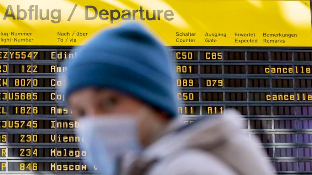 Ein Mann mit Mundschutz steht am Flughafen Berlin-Tegel vor der Anzeigetafel der Abflüge.
