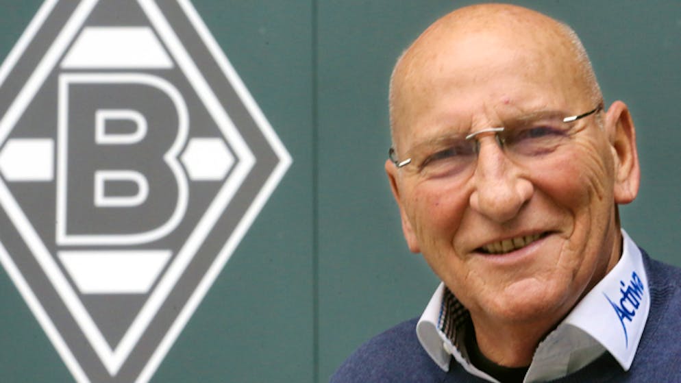 Der ehemalige Torwart von Borussia Mönchengladbach, Wolfgang Kleff, lächelt neben einem Wappen des Vereins.