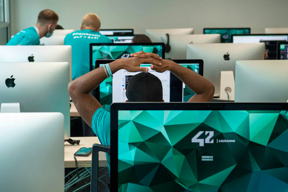 Ecole 42 Lausanne. Les élèves sont souvent seuls devant un écran, le but étant de résoudre des problèmes par soi-même afin de pouvoir aller plus loin. Leurs camarades relisent leurs travaux.