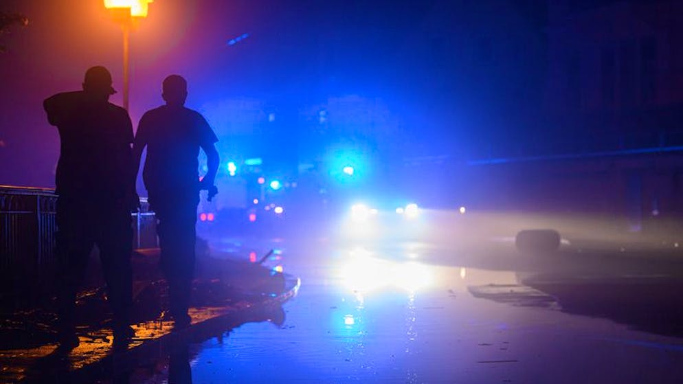 17.07.2021, Sachsen, Bad Schandau: Zwei Männer laufen am Rande einer von Wasser der Kirnitzsch überfluteten Straße entlang während im Hintergrund ein Feuerwehreinsatz läuft. Extreme Regenfälle von teils mehr als 100 Litern pro Quadratmeter innerhalb von 24 Stunden haben am Samstag in der Sächsischen Schweiz zu Überflutungen geführt. Foto: Robert Michael/dpa-Zentralbild/dpa +++ dpa-Bildfunk +++