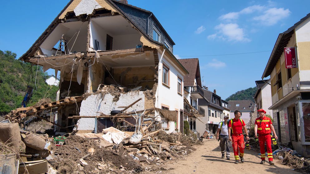 Helfer der Deutschen Lebensrettungsgesellschaft (DLRG) gehen an einem zerstörten Haus in Altenahr vorbei. Zahlreiche Häuser in dem Ort wurden komplett zerstört oder stark beschädigt.