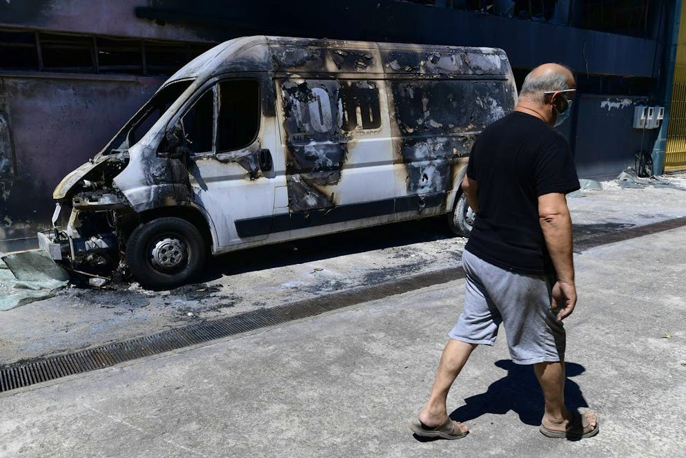 Un homme passe devant une camionnette incendiée, à Kryoneri, dans le nord d'Athènes, en Grèce, le dimanche 8 août 2021. Des centaines de pompiers en Grèce luttent toujours contre des incendies de forêt massifs qui ont détruit des étendues de forêt et provoqué des évacuations d'urgence d'un quartier populaire d'une île de vacances.
