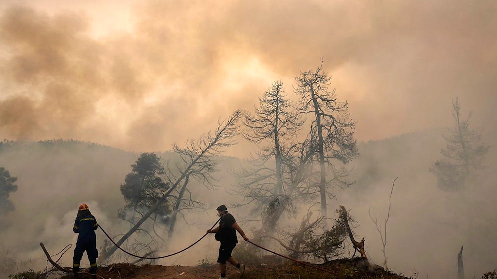 Zwei Männer versuchen im Dorf Ellinika auf der Insel Euböa die Flammen zu löschen. Inzwischen hat sich die Situation in Griechenland am Montag vorerst leicht entspannt.