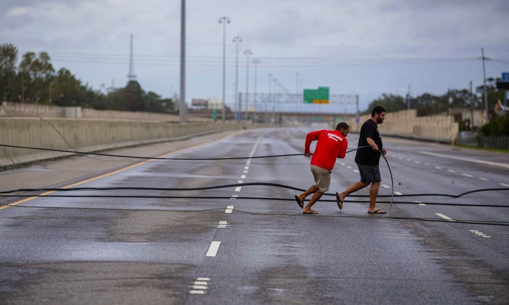 Employees with Kruger Roofing try and remove electrical wires that block traffic on Interstate 10 in both directions near Causeway Boulevard in Metairie, La., on Monday, Aug. 30, 2021. Wind from Hurricane Ida damaged the electrical infrastructure of Jefferson Parish. (David Grunfeld/The Advocate via AP)