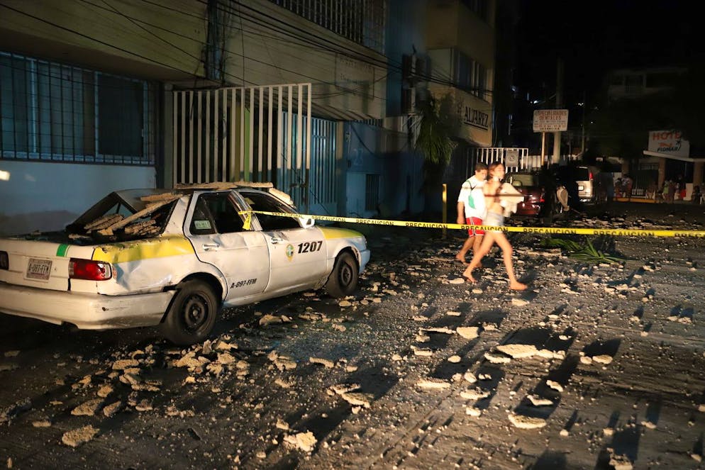Un couple passe devant un taxi qui a été endommagé par la chute de débris après un violent tremblement de terre à Acapulco, au Mexique, le mardi 7 septembre 2021.
