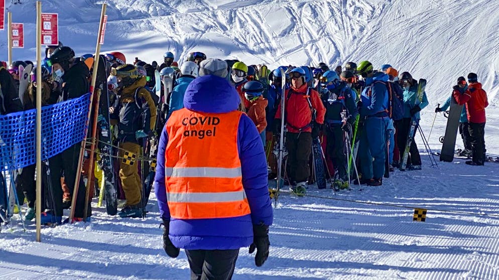 A ski lift staff identified as "Covid Angel" looking at skiers and snowboarders wearing protective face mask line up in a queue at the start of a ski lift during the coronavirus disease (COVID-19) outbreak, in the Alpine resort of Verbier, Switzerland, Saturday, January 16, 2021. (KEYSTONE/Sandra Hildebrandt)
