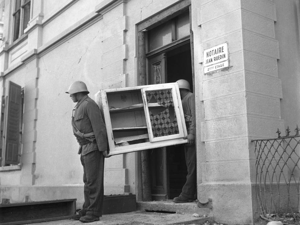 Zivilschuetzer tragen ein beschaedigtes Moebelstueck aus einem durch das Erdbeben beschaedigten Haus, aufgenommen am 25. Januar 1946 in Sierre, Kanton Wallis. (KEYSTONE/PHOTOPRESS-ARCHIV/Hermann Schmidli)