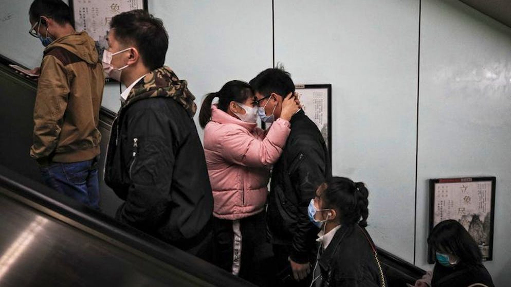 ARCHIV - 29.10.2020, China, Peking: Ein Paar, das Schutzmasken trägt, um die Ausbreitung des Coronavirus einzudämmen, umarmt sich beim Verlassen einer U-Bahn-Station während des morgendlichen Berufsverkehrs. In Zeiten von Kontaktsperren und Abstandsregeln wächst die Sehnsucht - die Sehnsucht nach Nähe, nach Körperkontakt, nach Umarmungen. Auch der diesjährige «Weltknuddeltag» steht im Zeichen von Corona. Foto: Andy Wong/AP/dpa +++ dpa-Bildfunk +++