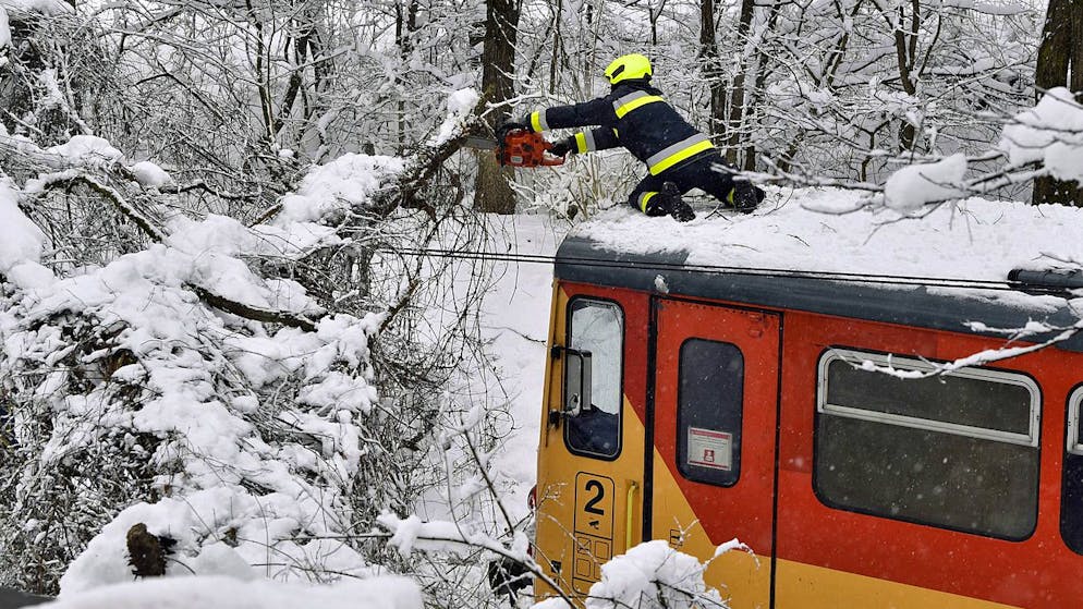 Bilder des Tages. Galionsfigur mit Kettensäge: Im ungarischen Szilvásvárad streckt sich ein Feuerwehrmann auf dem Dach eines Zugs, um einen Ast abzusägen, der unter der Schneelast heruntergebrochen ist und die Bahnstrecke blockiert. (25.1.2021)