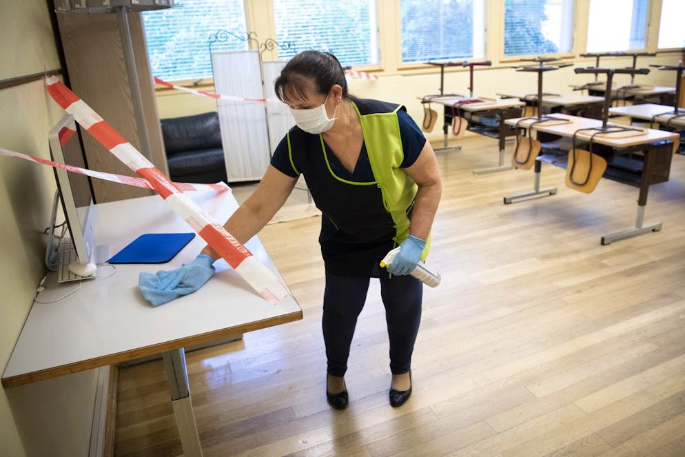 Une femme de menage portant un masque de protection desinfecte une salle de classe d' ecole de l'Etablissement Primaire de l'ecole vaudoise, EP Morges EST, le jour du retour des eleves lors de la pandemie de Coronavirus (Covid-19) ce lundi 11 mai 2020 au College de Chanel a Morges. Des le 11 mai, les eleves de l'ecole primaire et secondaire vaudoise reprennent l'ecole obligatoire par demi classe et un jour sur deux. (KEYSTONE/Laurent Gillieron)