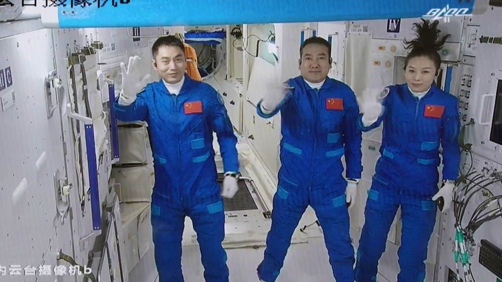In this photo released by Xinhua News Agency, screen image captured at Beijing Aerospace Control Center in Beijing, China, Saturday, Oct. 16, 2021 shows three Chinese astronauts, from left, Ye Guangfu, Zhai Zhigang and Wang Yaping waving after entering the space station core module Tianhe. China's Shenzhou-13 spacecraft carrying three Chinese astronauts on Saturday docked at its space station, kicking off a record-setting six-month stay as the country moves toward completing the new orbiting outpost. Chinese characters, left, read