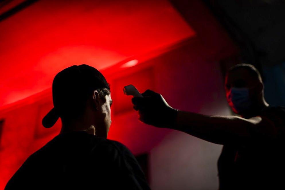 Un agent de securite prend la temperature d'un client devant la discotheque le D! Club lors de la crise du Coronavirus (Covid-19) le jeudi 2 juillet 2020 a Lausanne. Seulement 300 personnes peuvent danser par salle dans la discotheque lors d'une soiree et les personnes doivent egalement etre inscrites sur le Swiss Pass Night. (KEYSTONE/Jean-Christophe Bott)