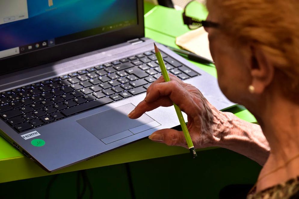 An elderly woman reads on a screen during a computer workshop in the