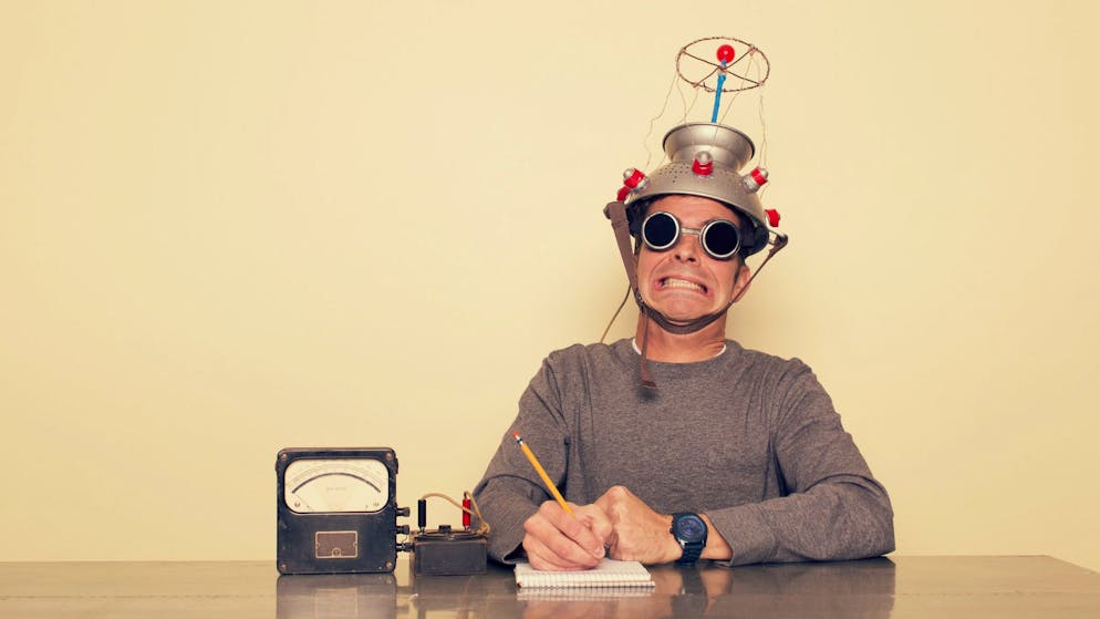 A man is testing the limits of the mind by placing a mind reading invention on his head trying to understand the brain. He is dressed in retro shirt and tie with safety goggles waiting to measure brain waves and understand the unknown.