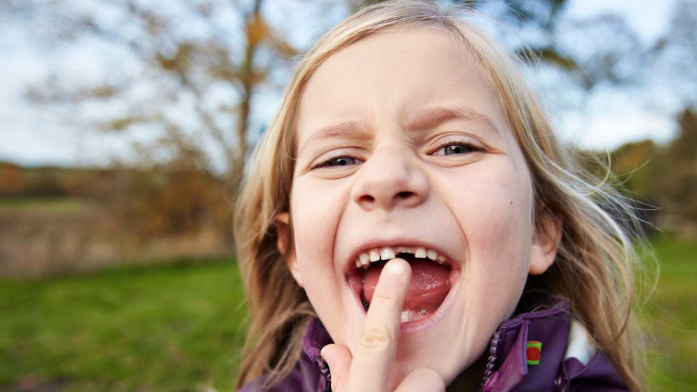 Portrait of cute blond girl showing new tooth at park during autumn
