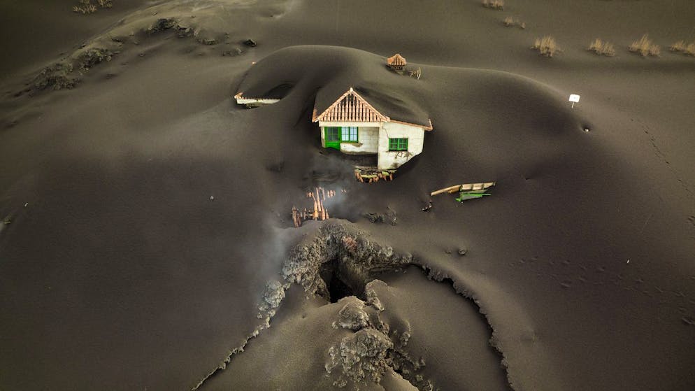 A fissure is seen next to a house covered with ash on the Canary island of La Palma, Spain, Wednesday, Dec.1 2021. A fissure that volcanologists believe spouted a gusher of lava left a gaping hole in front of house whose bottom floor was completely covered by a mountain of ash. A fresh stream of lava from volcano on Spain's La Palma threatened on Wednesday to engulf a parish church that has so far survived the eruption that shows no signs of relenting in its tenth week. (AP Photo/Emilio Morenatti)