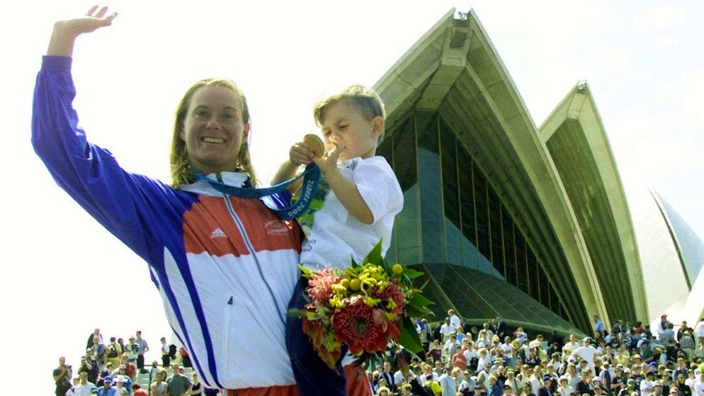 Winner of the women's Olympic triathlon Brigitte McMahon of Switzerland waves to the crowd from the winner's stand while her son Domiinic, 3, examines her gold medal Saturday, September 16, 2000. (AP Photo/David Guttenfelder)