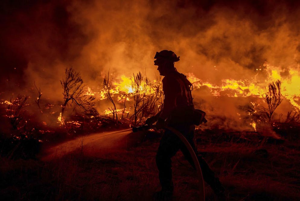 Un pompier arrose les zones de l'incendie de Dixie alors qu'il saute l'autoroute 395 au sud de Janesville, en Californie, le lundi 16 août 2021.