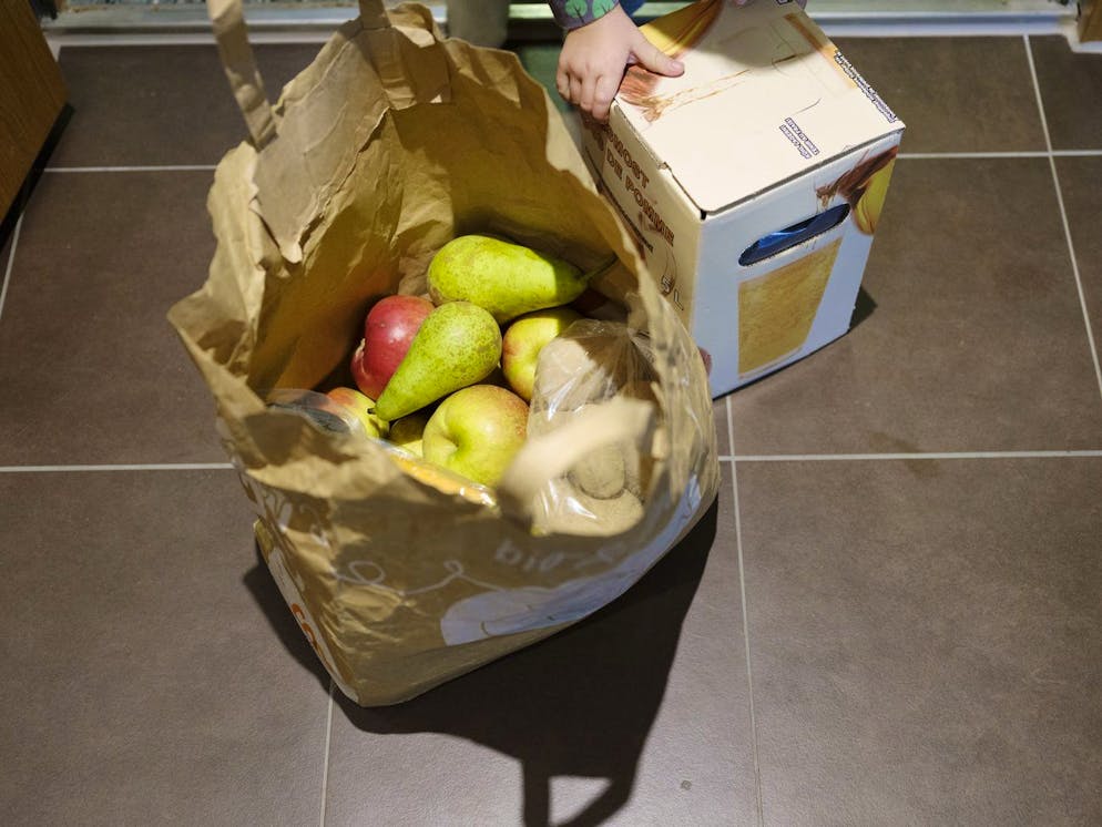 Ein Kleinkind probiert einen Karton mit Apfelsaft zu heben, das zusammen mit einer Papiertragtasche mit Obst vor die Wohnungstuer der Familie, die sich in Quarantaene befindet, geliefert wurde, fotografiert am 6. November 2020 in Zuerich. (KEYSTONE/Christian Beutler)