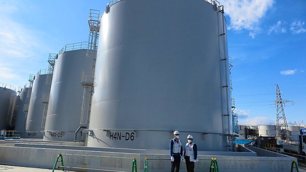 ARCHIV - Zwei Mitarbeiter des Betreiberkonzerns Tepco stehen vor riesigen Tanks, in denen verstrahltes Wasser, das bei der andauernden Kühlung der beschädigten Reaktoren von Fukushima anfällt, gelagert wird. Foto: Lars Nicolaysen/dpa