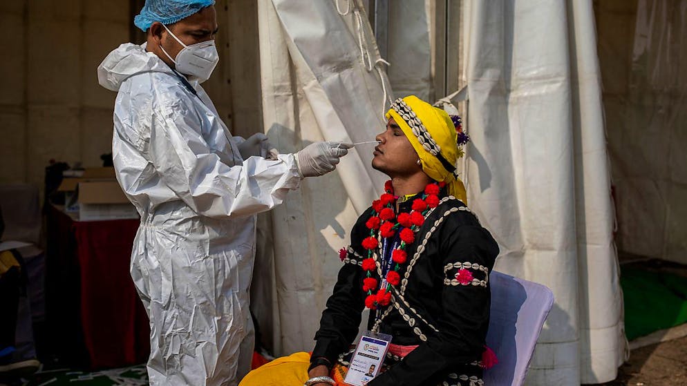 ARCHIV - Ein Mitarbeiter des Gesundheitswesen in Indien entnimmt einem Mann einen Abstrich für einen Corona-Test. Foto: Altaf Qadri/AP/dpa