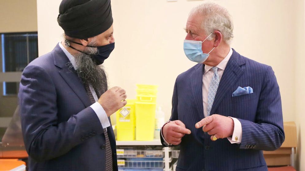 Der britische Prinz Charles (r), Prinz von Wales, unterhält sich mit Inderjit Singh, Chefapotheker, im Rahmen seines Besuchs im Queen Elizabeth Krankenhaus. Das Königspaar möchte sich bei den Freiwilligen bedanken, die an einer klinischen Studie für die Impfungen gegen das Coronavirus teilnehmen. Foto: Molly Darlington/PA Wire/dpa