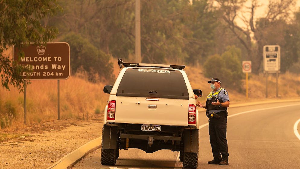 Police talk to residents hoping to return to their properties at a road block on Great Northern Highway in Perth, Tuesday, February 2, 2021. An out-of-control bushfire burning near the Perth Hills has engulfed at least three homes and is threatening more, with locals in a large swathe of the region told it is too late to leave. (AAP Image/Richard Wainwright) NO ARCHIVING