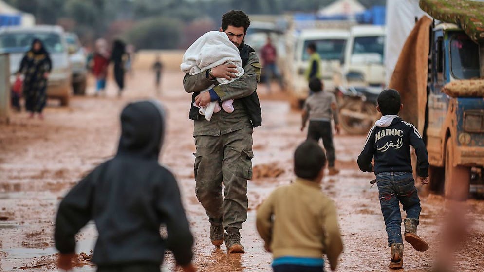 ARCHIV - Ein Syrer trägt sein Baby in einem Behelfslager für Familien, die aus Idlib vertrieben wurden. Foto: Anas Alkharboutli/dpa