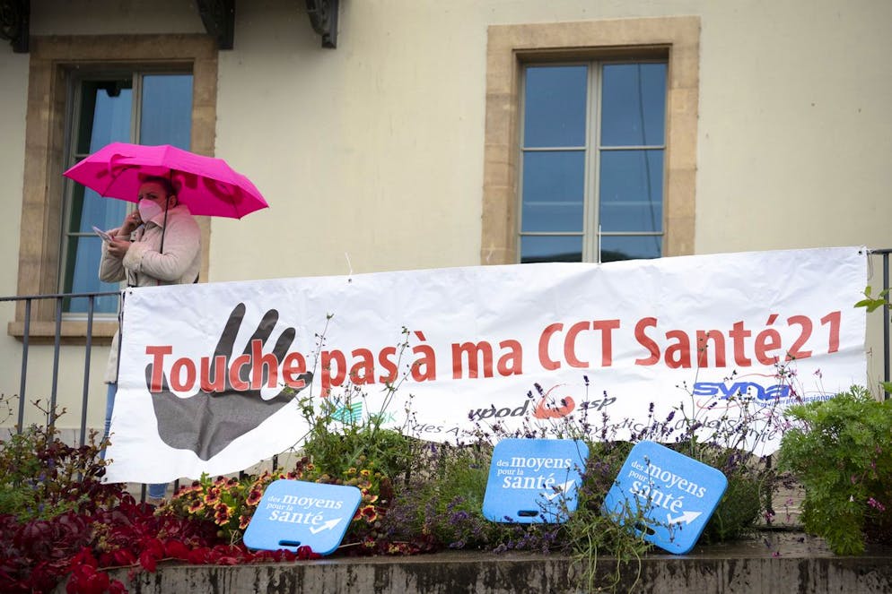Une personne portant un masque de protection facial passe derriere une banderole des syndicats Syna, SSP et ASI lors du lancement de la semaine de protestation "Maintenant plus que jamais!" afin d'ameliorer les conditions de travail du personnel de la sante lors de la 2eme vague de la pandemie de Coronavirus (Covid-19) ce lundi 26 octobre 2020 devant l'Hopital Pourtales du Reseau hospitalier neuchatelois, RhNE, a Neuchatel. (KEYSTONE/Laurent Gillieron)