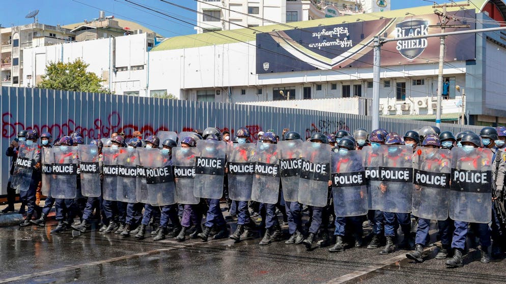 Polizisten mit Schutzschilden blockieren eine Demonstration an einer Kreuzung in Mandalay.