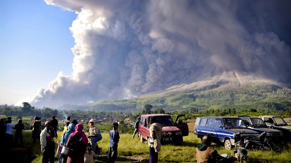 People watch as Mount Sinabung spews volcanic material during an eruption in Karo, North Sumatra, Indonesia, Tuesday, March 2, 2021. The 2,600-metre (8,530-feet) volcano erupted Tuesday, sending volcanic materials a few thousand meters into the sky and depositing ash on nearby villages. (AP Photo)