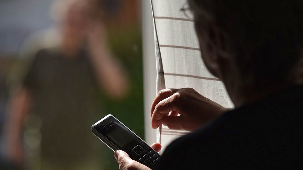 ILLUSTRATION - 05.07.2016, Bayern, Garmisch-Partenkirchen: ARCHIV - Eine Frau steht mit einem Telefon am Fenster, vor dem ein Mann steht (gestellte Szene). Opfer von Stalking sollen nach Ansicht des Bundesjustizministeriums künftig eine bessere rechtliche Handhabe gegen ihre Peiniger haben. Das Kabinett soll am 03.02.2021 einen Bericht des Ministeriums zu möglichem Reformbedarf bei den aktuellen Anti-Stalking-Regeln verabschieden. Foto: Angelika Warmuth/dpa +++ dpa-Bildfunk +++ (KEYSTONE/DPA/Angelika Warmuth)
