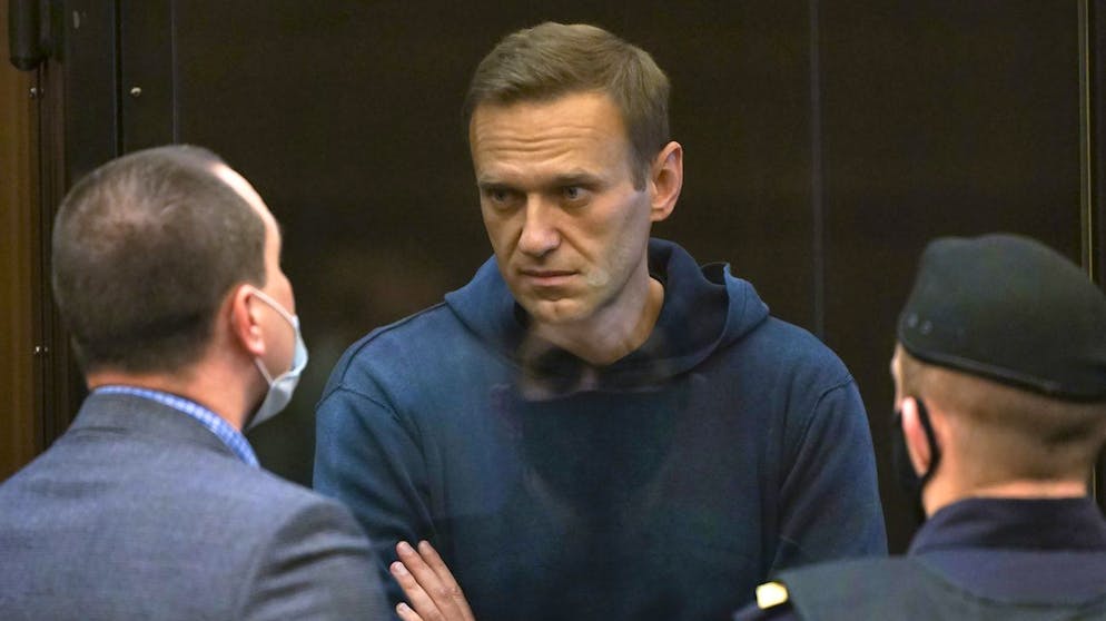 In this handout photo provided by Moscow City Court Russian opposition leader Alexei Navalny talks to one of his lawyers, left, while standing in the cage during a hearing to a motion from the Russian prison service to convert the suspended sentence of Navalny from the 2014 criminal conviction into a real prison term in the Moscow City Court in Moscow, Russia, Tuesday, Feb. 2, 2021. (Moscow City Court via AP)
