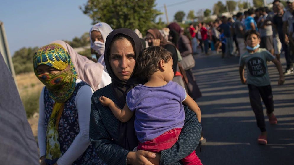 A woman holds a baby as she waits with other migrants in a queue for food distribution near Mytilene town, on the northeastern island of Lesbos, Greece, Saturday, Sept. 12, 2020. Greek authorities have been scrambling to find a way to house more than 12,000 people left in need of emergency shelter on the island after the fires deliberately set on Tuesday and Wednesday night gutted the Moria refugee camp. (AP Photo/Petros Giannakouris)