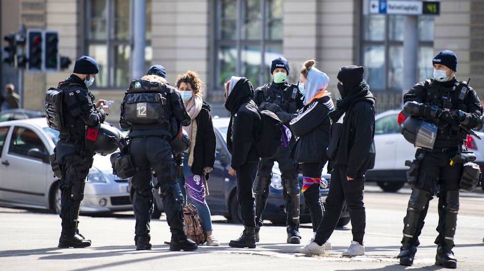 Polizisten kontrollieren demonstrierende Menschen mit dem Slogan