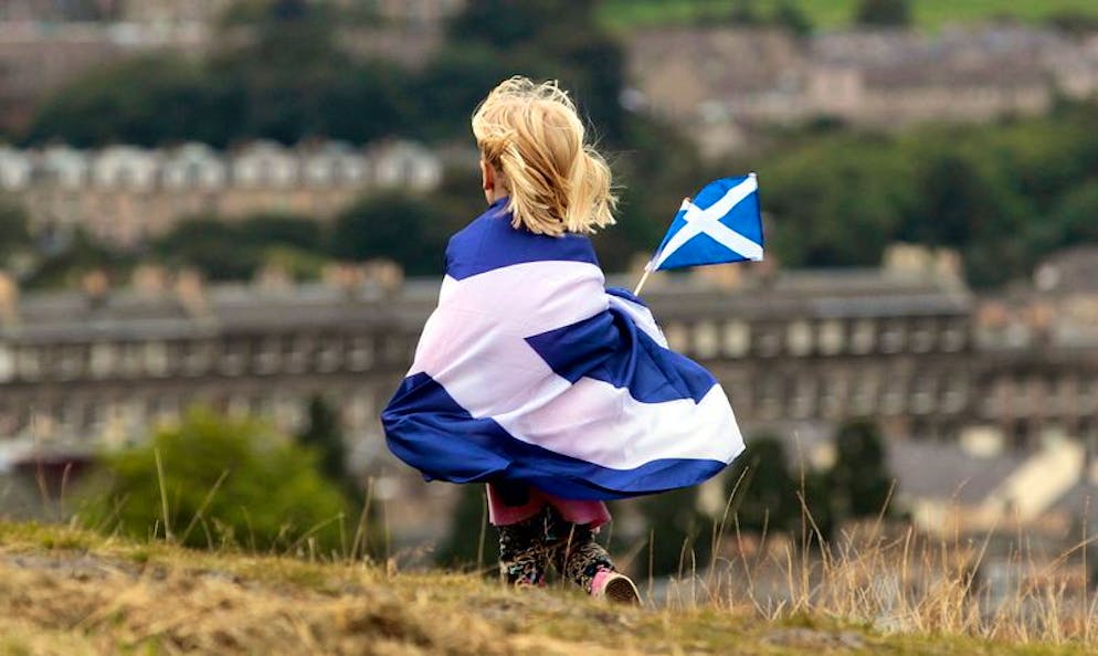 ARCHIV - 21.09.2013, Großbritannien, Edinburgh: Ein Kind, in eine schottische Flagge gehüllt, geht während einer Demonstration für die schottische Unabhängigkeit über einen Rasen. (zu dpa
